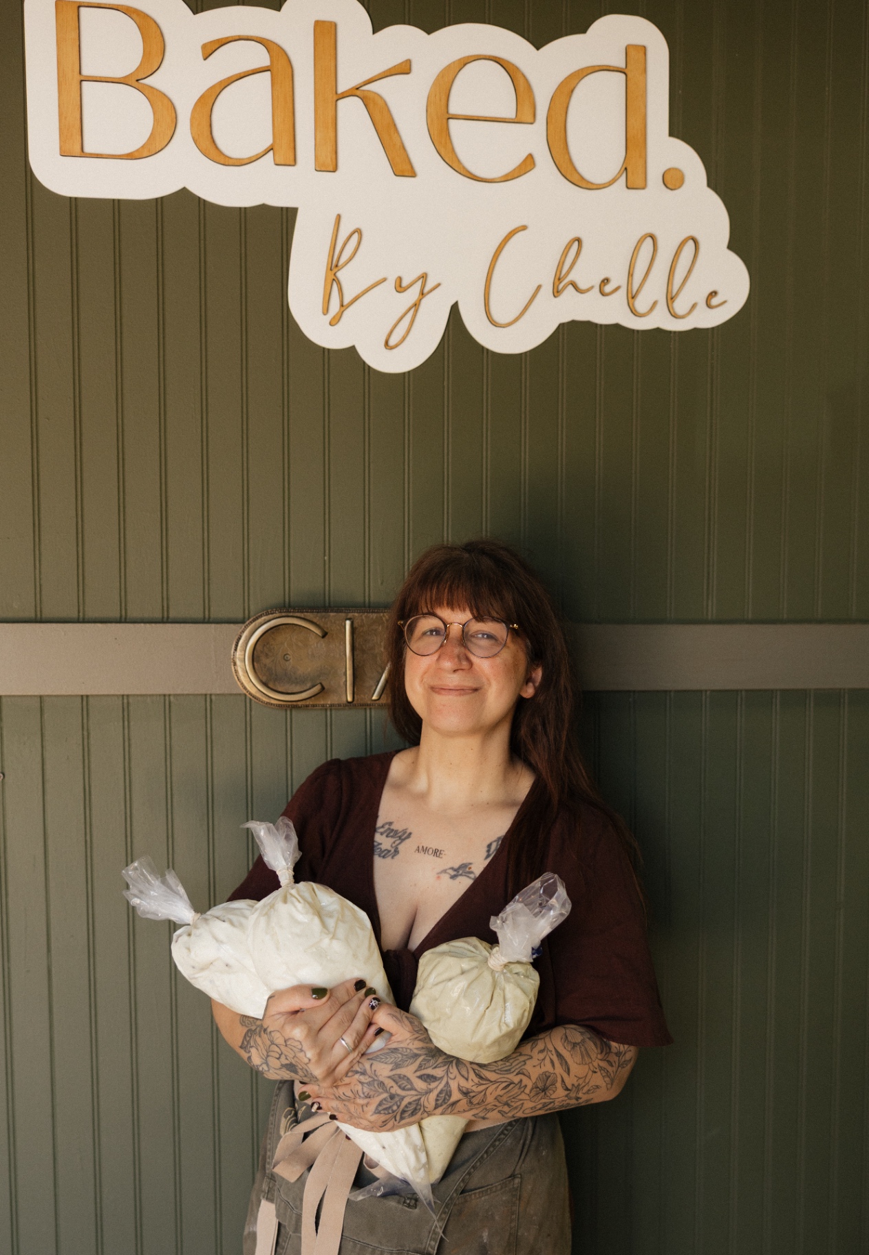 Chelle beneath the Baked. By Chelle sign holding bags of fresh pastry cream